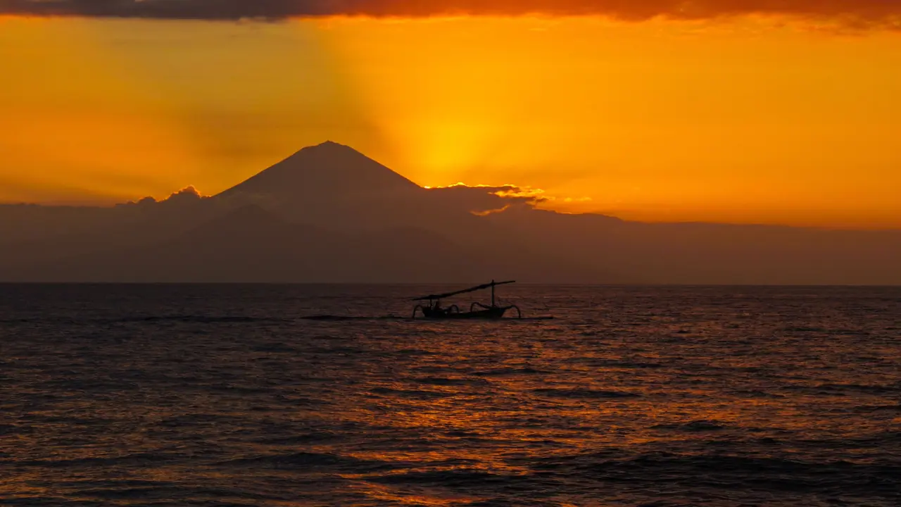Fishing boat on a still sea with Mount Agung against a golden sky