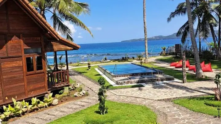 The wooden house at Wooden House Candidasa with its garden, the pool and the sea behind the palms